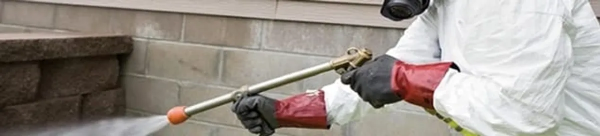 Pest control technician applying exterior insect treatment along a home foundation in Baltimore, MD