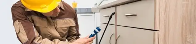 Roach exterminator applying treatment under kitchen cabinets in Baltimore, MD