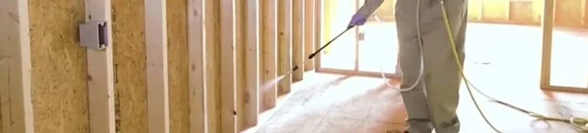 Termite treatment technician applying spray along framing and unfinished walls in Baltimore, MD
