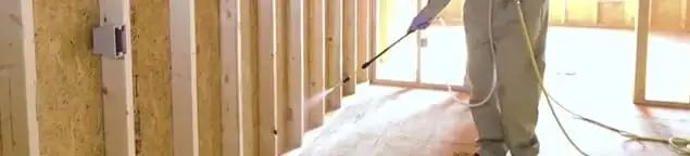Termite treatment technician applying spray along framing and unfinished walls in Baltimore, MD